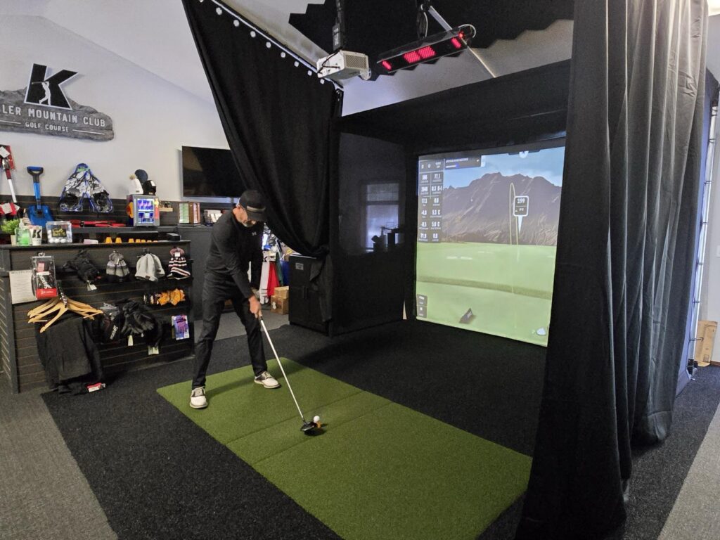 A golfer mid-swing in the indoor golf simulator bay at the Kahler Mountain Club pro shop.